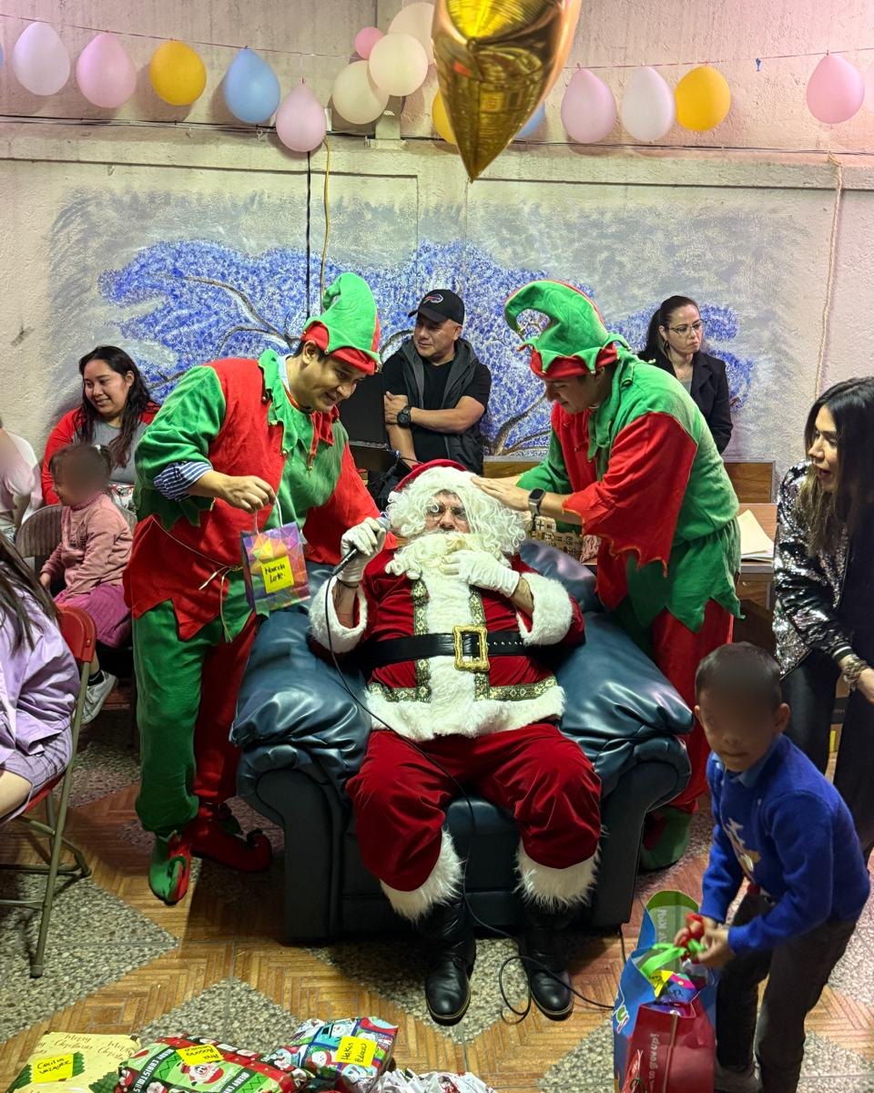 Santa Claus sentado en un sillón, acompañado por dos duendes, durante la posada de una casa hogar