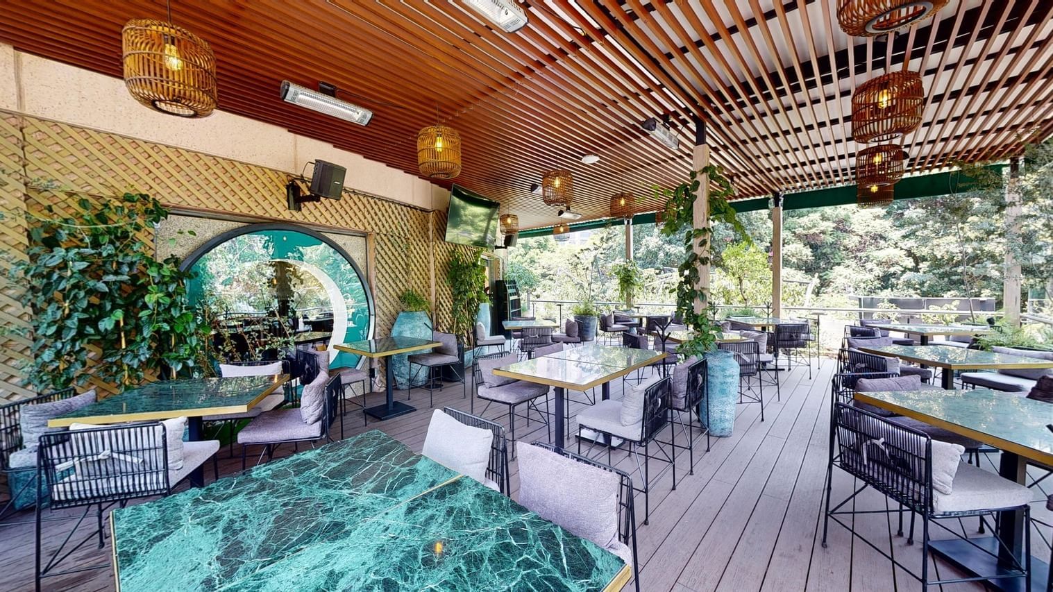 Terraza de Santino Reforma con mesas de mármol verde, pérgola de madera y vegetación
